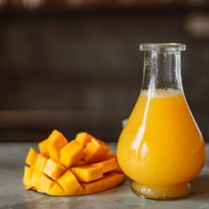 A refreshing and vibrant mango juice served in a clear glass bottle next to ripe mangos.